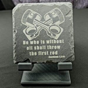 Slate coaster engraved with crossed pistons and the saying, "He who is without oil shall throw the first rod"